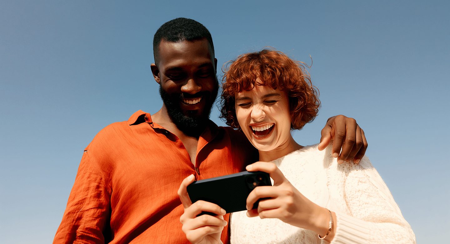 Couple laughing sharing smartphone outdoors